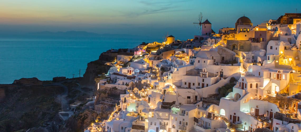 Greek island with white buildings lit up at dusk